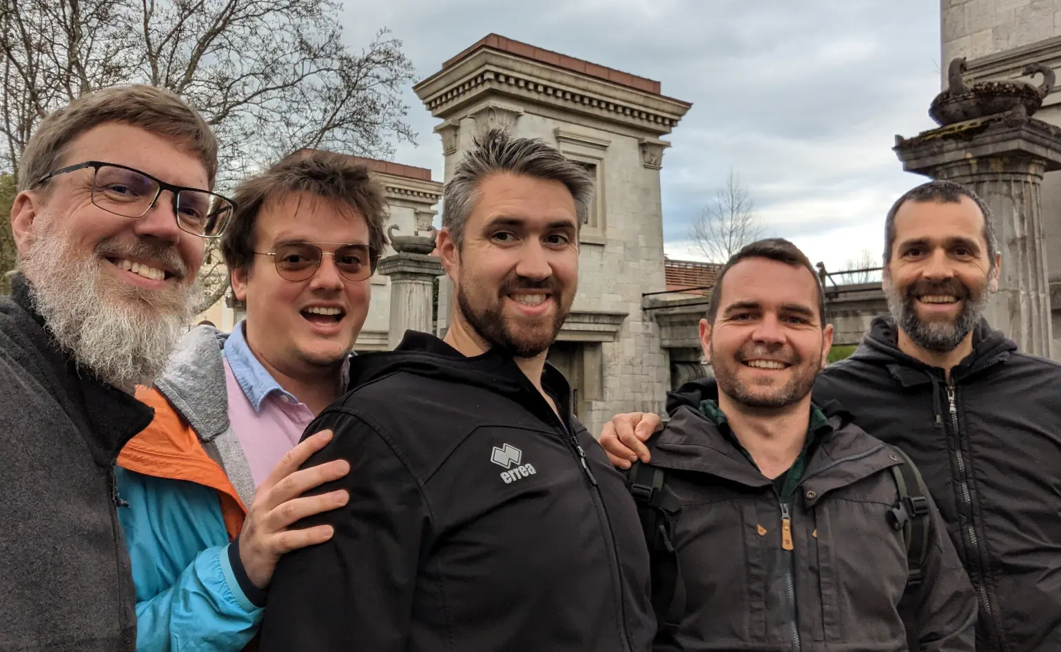 5 men smiling for the camera outside against classic pillar and walls
